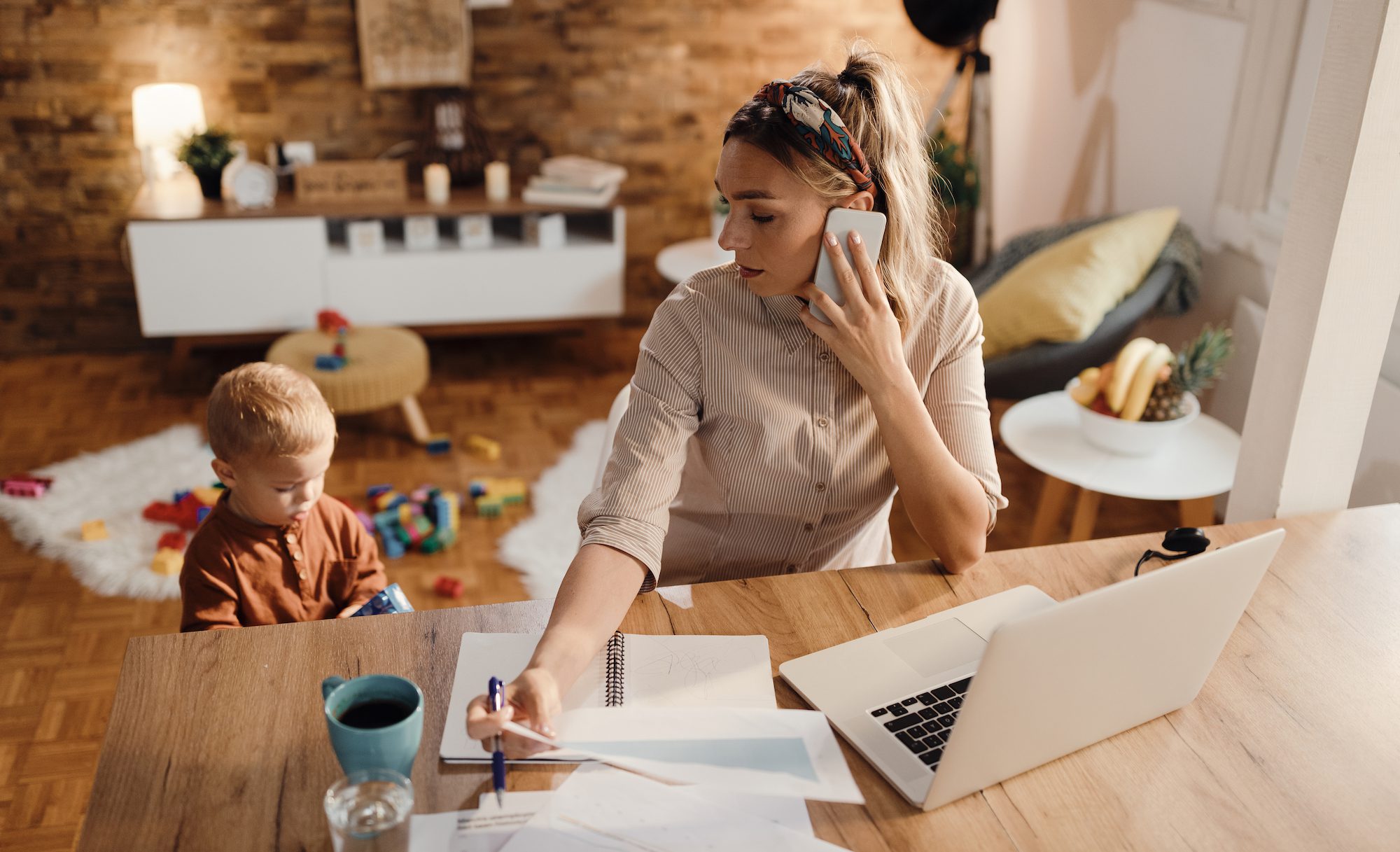 Female entrepreneur talking on the phone while being with her son at home.